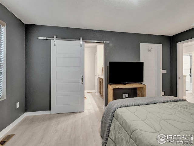 bedroom with a barn door, baseboards, ensuite bathroom, light wood-type flooring, and visible vents