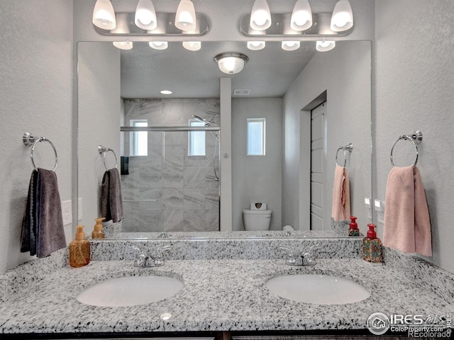 bathroom with double vanity, a sink, a stall shower, and toilet