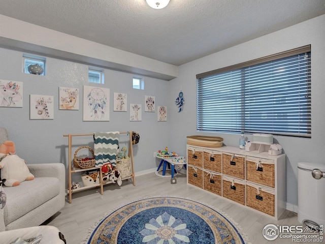 recreation room featuring a textured ceiling, baseboards, and wood finished floors