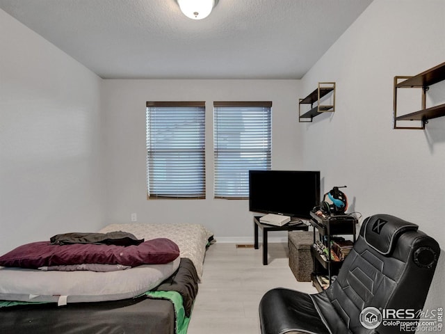bedroom featuring baseboards, a textured ceiling, and light wood finished floors