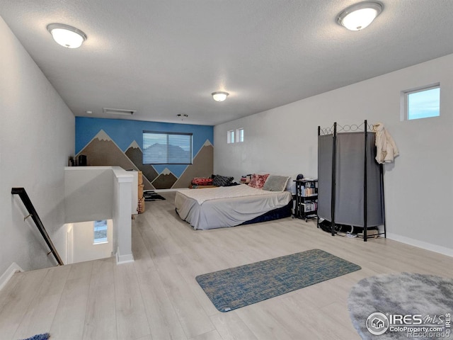 bedroom with a textured ceiling, baseboards, multiple windows, and wood finished floors