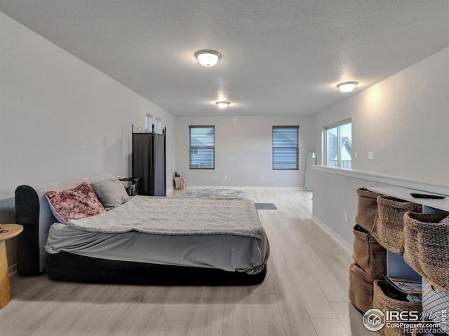 bedroom featuring baseboards, a textured ceiling, and light wood-style flooring