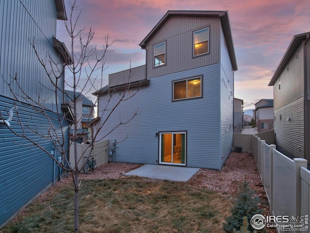 back of property at dusk with a fenced backyard, central air condition unit, a lawn, and a patio area