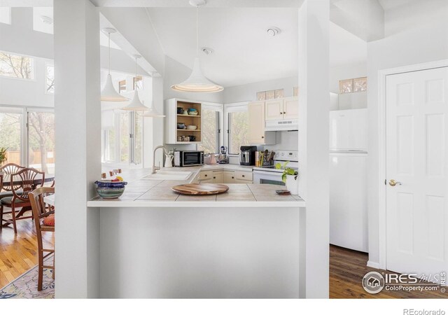 kitchen featuring white appliances, a sink, tile counters, under cabinet range hood, and wood finished floors