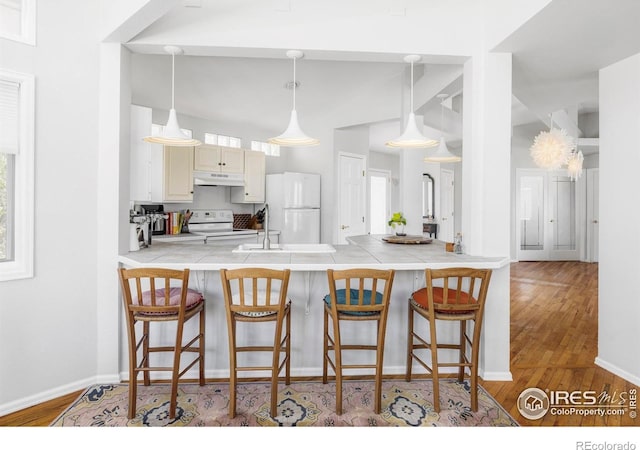 kitchen featuring white appliances, a peninsula, wood finished floors, and a breakfast bar
