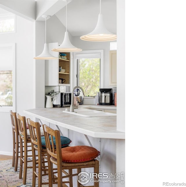 kitchen featuring a sink, a kitchen bar, open shelves, and white cabinets