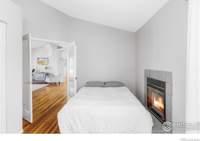 bedroom featuring wood finished floors, a tile fireplace, and lofted ceiling