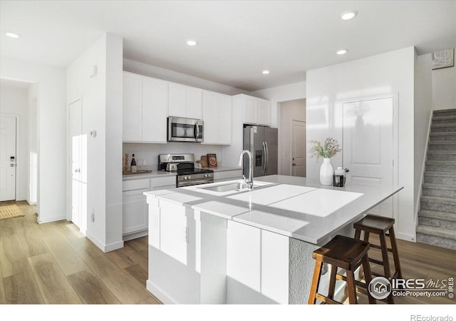 2260 Crescent Cir, Erie, CO 80026 - kitchen featuring appliances with stainless steel finishes, a sink, an island with sink, light wood-style floors, and white cabinetry