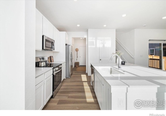 2260 Crescent Cir, Erie, CO 80026 - kitchen with appliances with stainless steel finishes, a sink, a kitchen island with sink, light wood-style flooring, and white cabinets