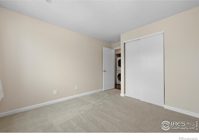 6385 Oak St Unit 301, Arvada, CO 80004 - unfurnished bedroom featuring stacked washer / dryer, carpet floors, a closet, and a textured ceiling