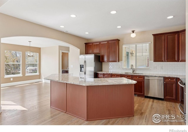 3530 Willow Rd, Frederick, CO 80504 - kitchen featuring decorative backsplash, arched walkways, a center island, light wood-style floors, and stainless steel appliances