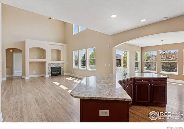 3530 Willow Rd, Frederick, CO 80504 - kitchen featuring light stone counters, hanging light fixtures, light wood finished floors, arched walkways, and a tile fireplace
