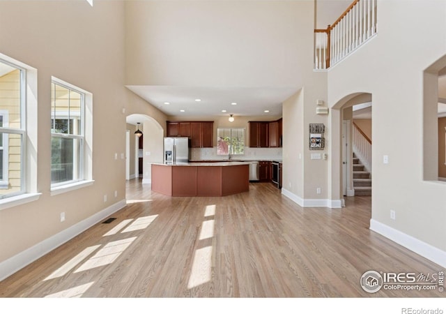3530 Willow Rd, Frederick, CO 80504 - unfurnished living room with visible vents, a sink, a towering ceiling, arched walkways, and light wood finished floors