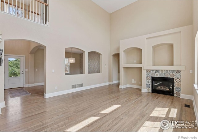 3530 Willow Rd, Frederick, CO 80504 - unfurnished living room featuring visible vents, a tiled fireplace, light wood-type flooring, baseboards, and a high ceiling