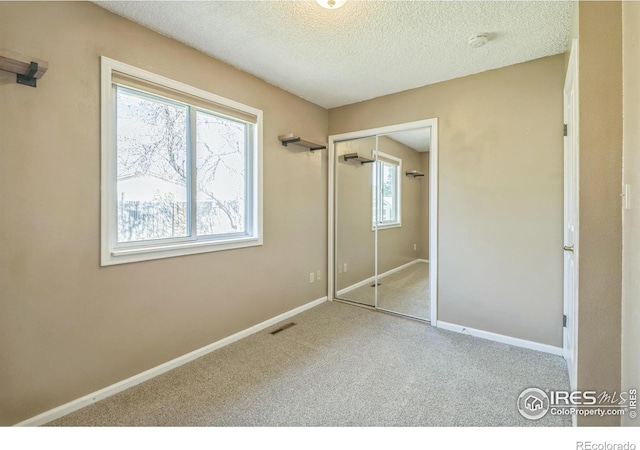 unfurnished bedroom featuring a textured ceiling, carpet, baseboards, visible vents, and a closet