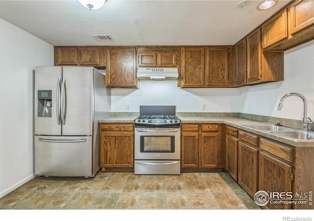 kitchen with brown cabinets, appliances with stainless steel finishes, a sink, under cabinet range hood, and visible vents