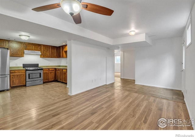 kitchen with brown cabinets, stainless steel appliances, open floor plan, a ceiling fan, and under cabinet range hood
