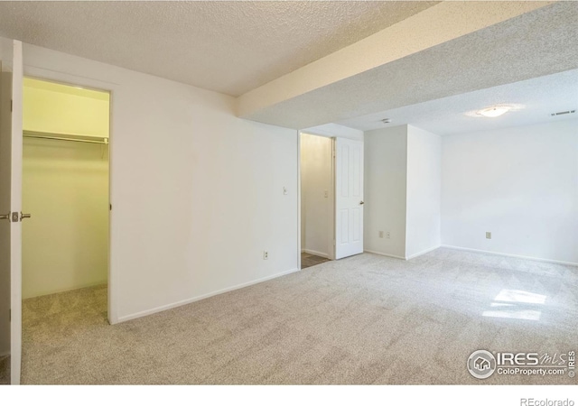 interior space with carpet floors, a textured ceiling, a walk in closet, and baseboards