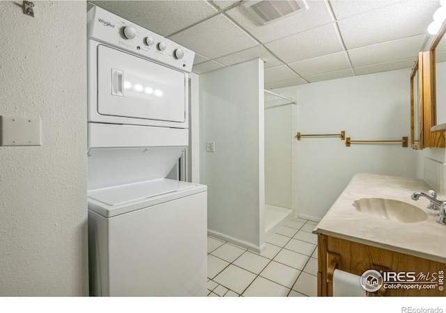clothes washing area featuring laundry area, visible vents, stacked washing maching and dryer, a sink, and light tile patterned floors
