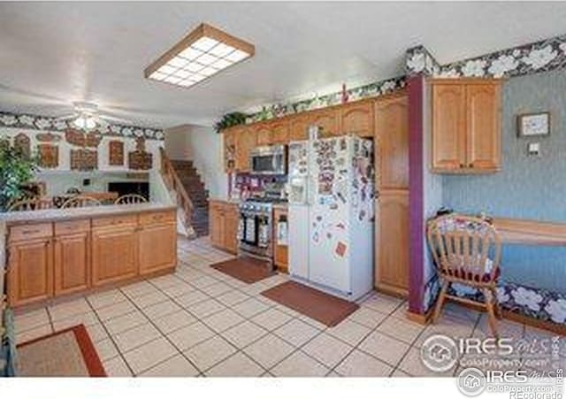 kitchen featuring stainless steel appliances, brown cabinets, light countertops, a ceiling fan, and light tile patterned floors