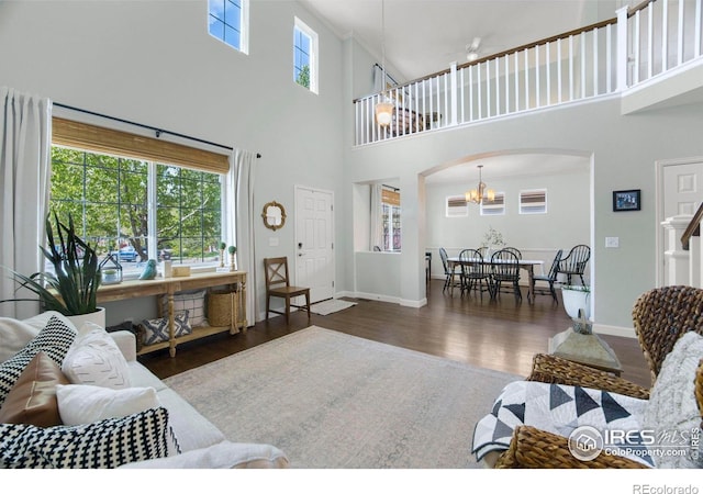 living room with wood finished floors, a towering ceiling, a chandelier, arched walkways, and baseboards