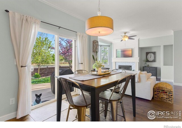 dining space with wood finished floors, crown molding, ceiling fan, baseboards, and a glass covered fireplace