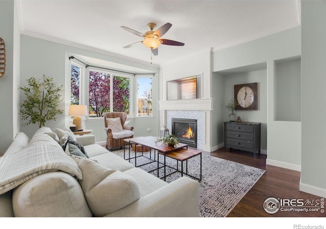 living area featuring a ceiling fan, baseboards, a fireplace, and crown molding