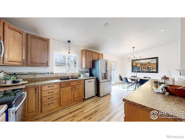 kitchen with hanging light fixtures, a notable chandelier, appliances with stainless steel finishes, a sink, and light wood finished floors