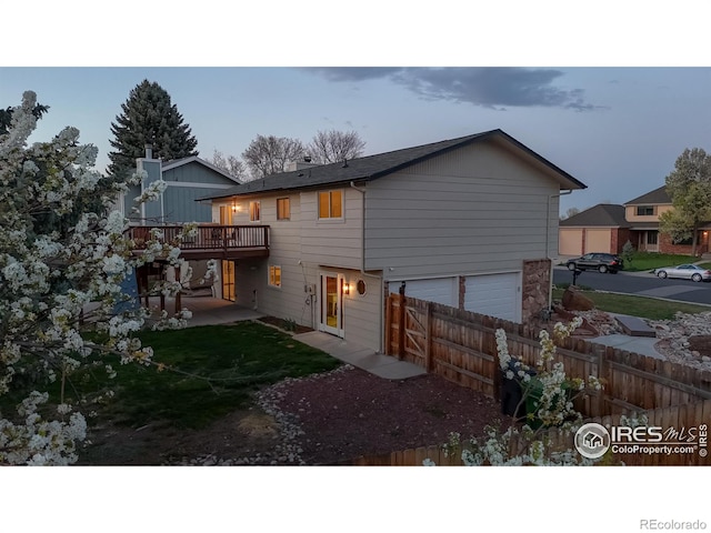 rear view of property featuring a deck, an attached garage, fence, and a patio