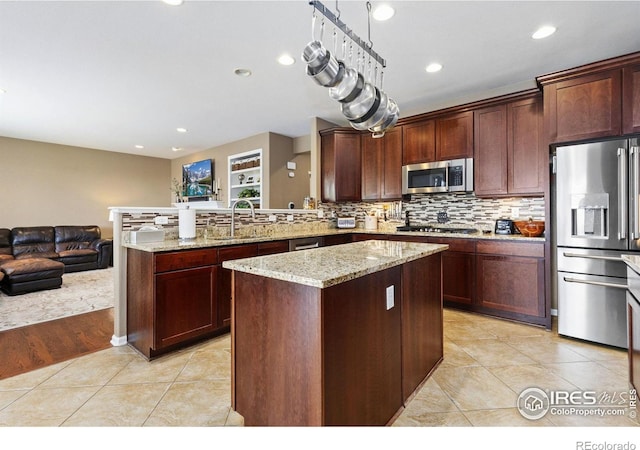 kitchen with a center island, light stone countertops, a sink, open floor plan, and stainless steel appliances