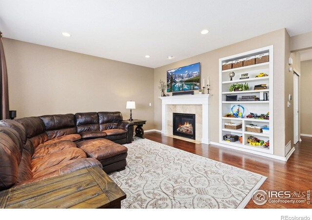 living area featuring built in features, a tiled fireplace, recessed lighting, baseboards, and wood finished floors