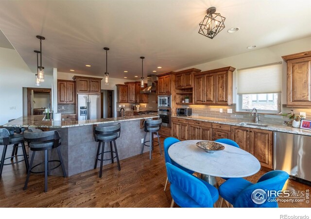 5751 Last Pointe Dr, Windsor, CO 80550 - kitchen featuring stainless steel appliances, a sink, wall chimney exhaust hood, brown cabinetry, and recessed lighting