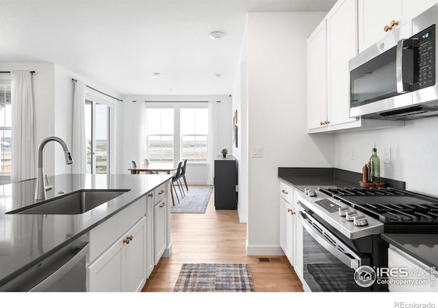 840 Clover Loop, Lafayette, CO 80026 - kitchen featuring dark countertops, a sink, white cabinets, light wood finished floors, and stainless steel appliances