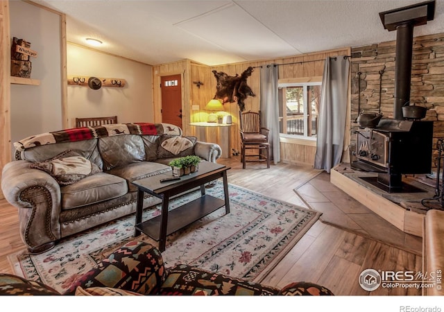 living room featuring a textured ceiling, vaulted ceiling, a wood stove, wood walls, and wood finished floors