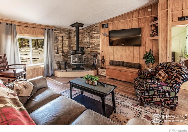 living room featuring wooden walls, a wood stove, wood finished floors, and lofted ceiling