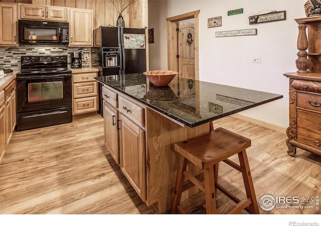 kitchen featuring light brown cabinets, a breakfast bar area, light wood-style flooring, decorative backsplash, and black appliances