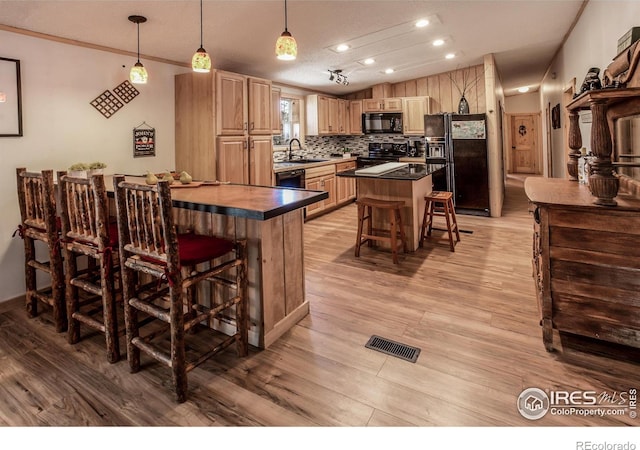 kitchen with visible vents, dark countertops, a breakfast bar, light wood-type flooring, and black appliances