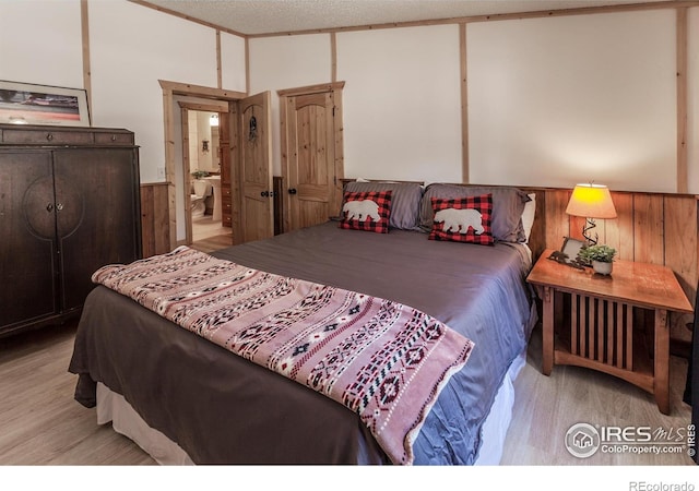 bedroom with a wainscoted wall, a textured ceiling, wood walls, and wood finished floors