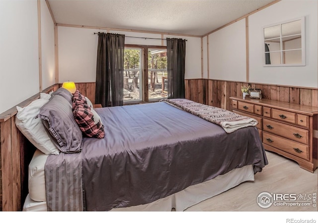 bedroom featuring a wainscoted wall, light wood finished floors, wood walls, and a textured ceiling