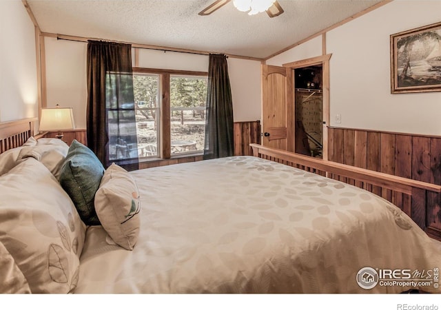 bedroom featuring wood walls, lofted ceiling, ceiling fan, a textured ceiling, and a wainscoted wall