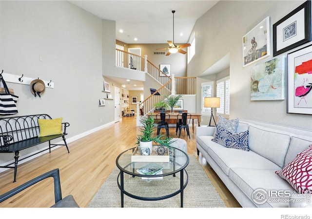 living area with ceiling fan, stairs, wood finished floors, a high ceiling, and recessed lighting