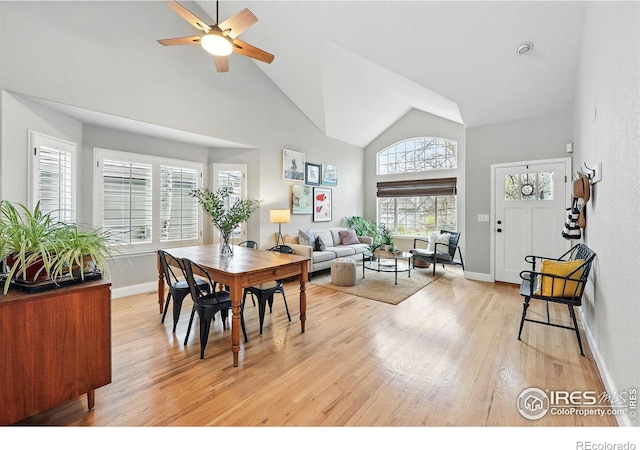 dining room with light wood-style floors, baseboards, ceiling fan, and high vaulted ceiling