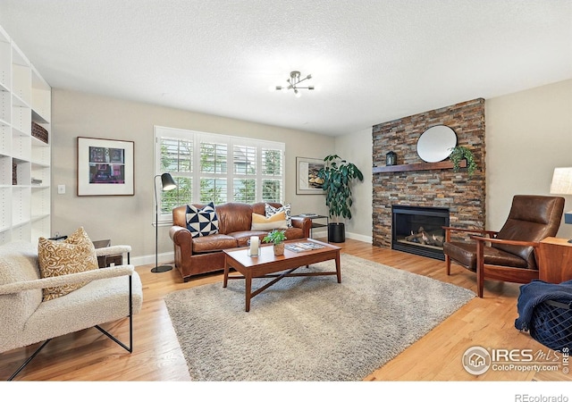 living area featuring light wood-style floors, a textured ceiling, baseboards, and a stone fireplace