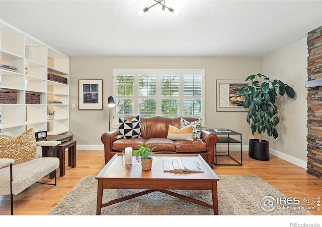 living room featuring baseboards, a textured ceiling, and light wood-style flooring