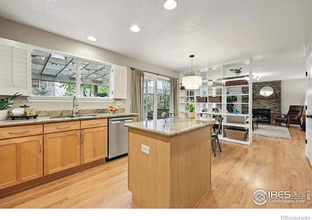 kitchen featuring a sink, light wood finished floors, a fireplace, stainless steel dishwasher, and a kitchen island