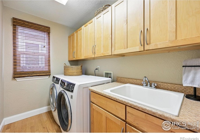 laundry area with light wood-type flooring, cabinet space, a sink, baseboards, and washer and clothes dryer