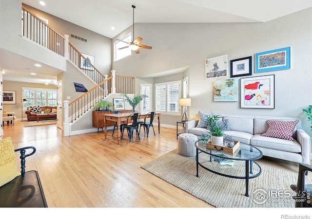 living area featuring ceiling fan, visible vents, wood finished floors, stairway, and a high ceiling
