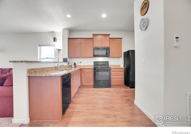 kitchen featuring light wood-type flooring, a sink, light stone counters, black appliances, and a peninsula