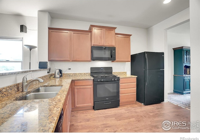 kitchen with a sink, light wood-style floors, light stone countertops, and black appliances