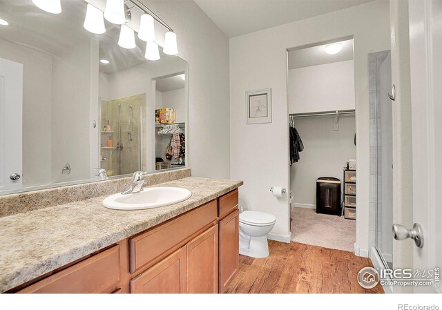 bathroom with a walk in closet, vanity, toilet, wood finished floors, and a stall shower
